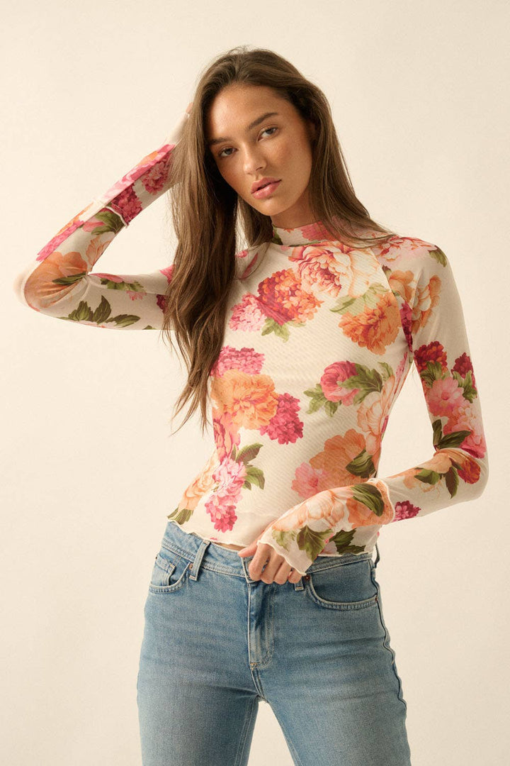 Woman wearing a floral mesh long-sleeve top and jeans on a plain background