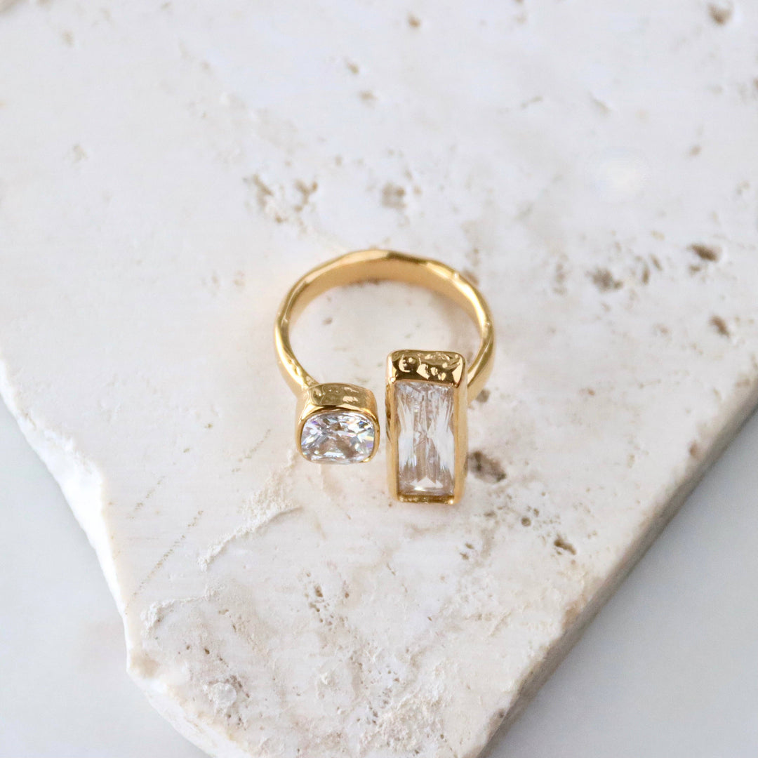 Gold ring with two geometric CZ gemstones on a marble surface