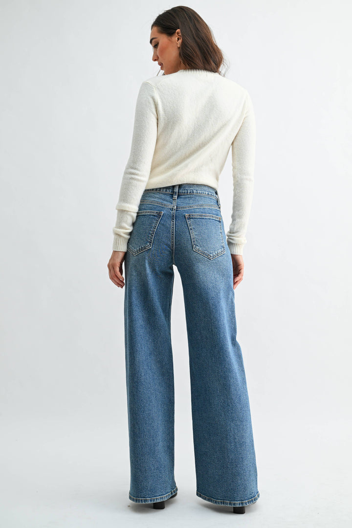 Woman wearing medium wash  blue wide leg jeans and a white sweater on a white background