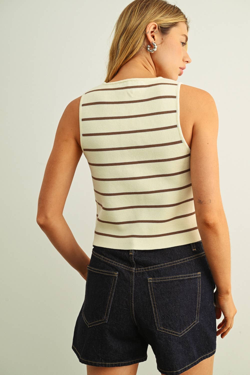 Woman wearing a striped sleeveless top and denim shorts on a plain background