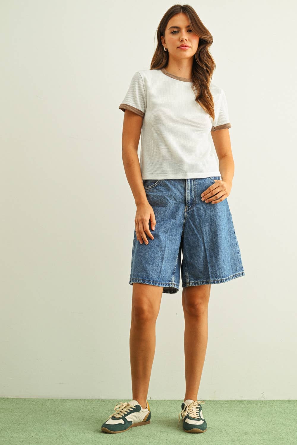 Woman wearing a white t-shirt and blue denim shorts on a plain background