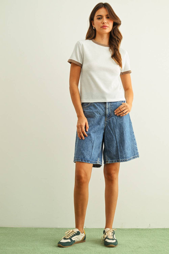 Woman wearing a white t-shirt and blue denim shorts on a plain background