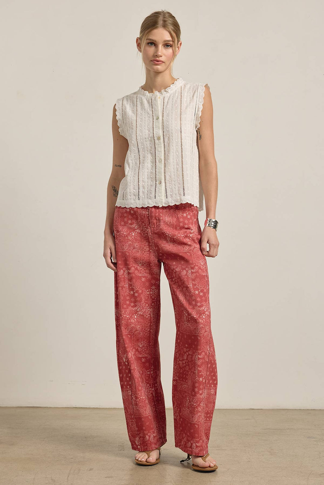 Woman wearing a white sleeveless top and red patterned pants against a plain background