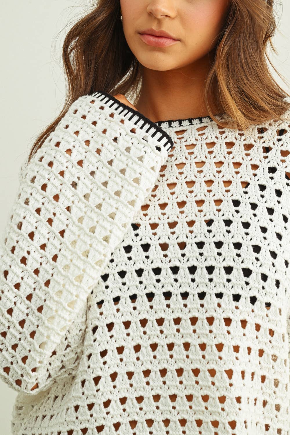 Close-up of a woman wearing a white crochet top with black accents.