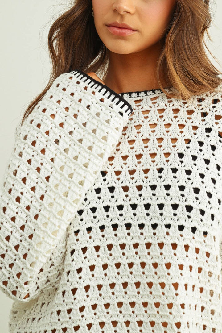 Close-up of a woman wearing a white crochet top with black accents.
