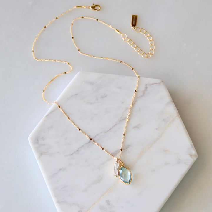 Gold necklace with a blue teardrop pendant on a marble surface