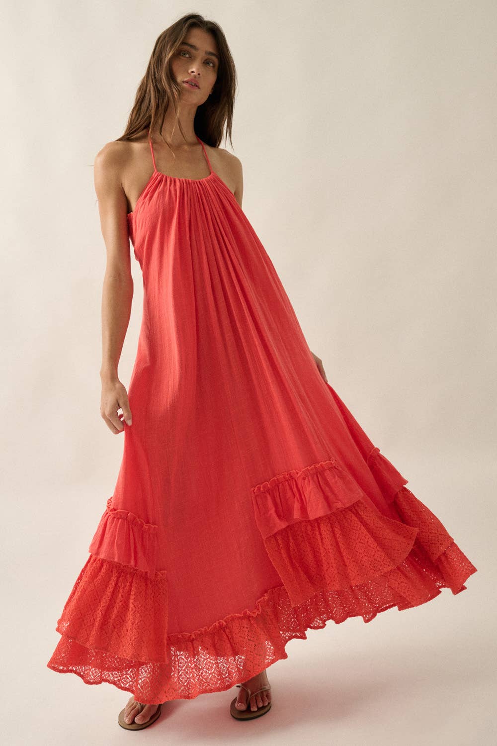 Woman wearing a coral pink halter summer dress with ruffled layers on a plain background