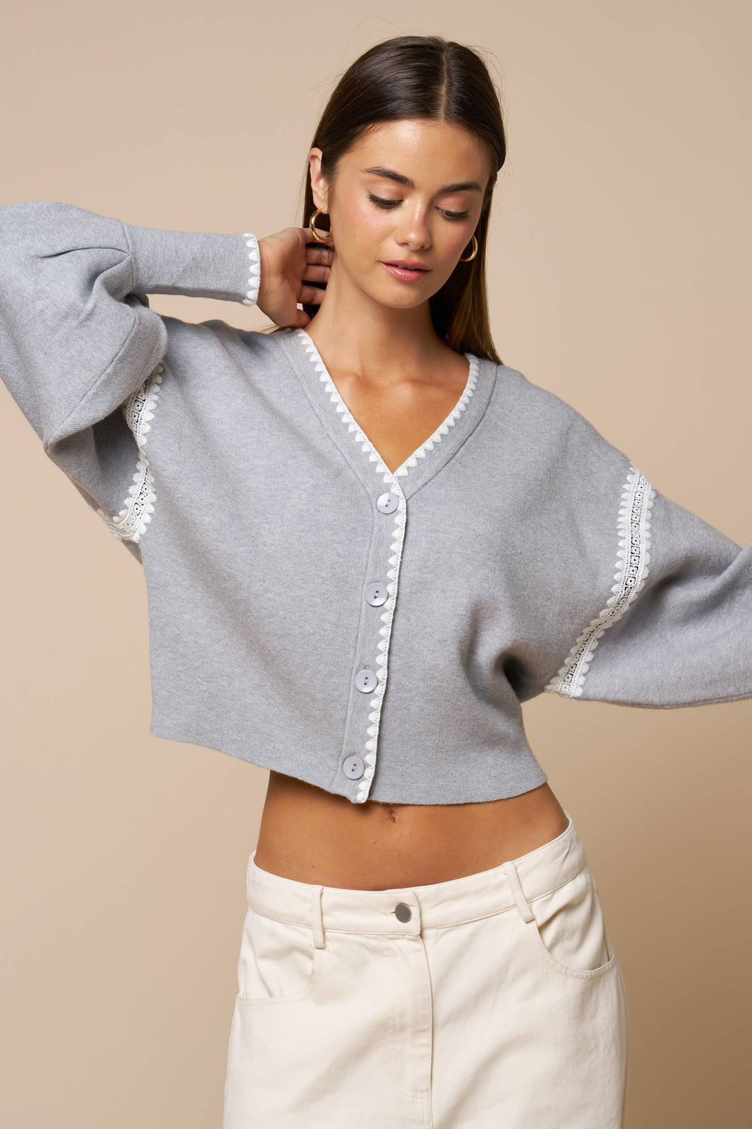 Woman wearing a gray cardigan with lace trim on a beige background