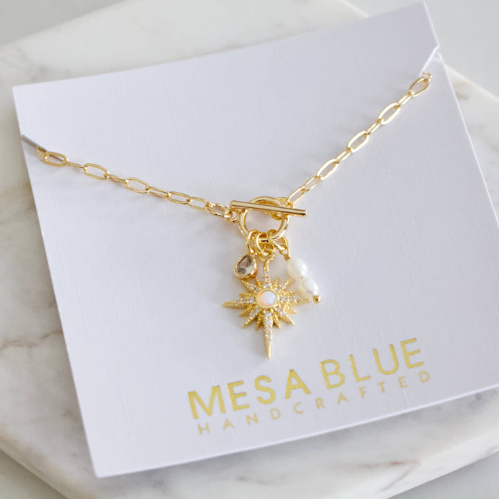 Gold necklace with charms on a Mesa Blue card