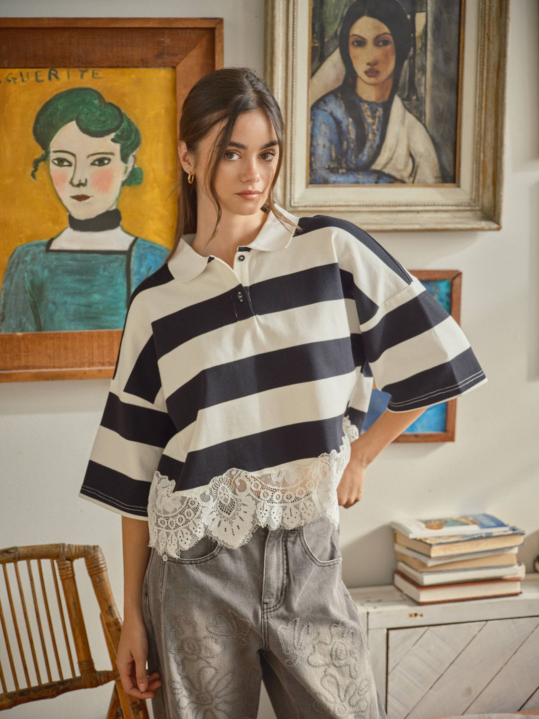Woman wearing a black and white striped polo shirt with lace details in a room with framed artwork on the wall.