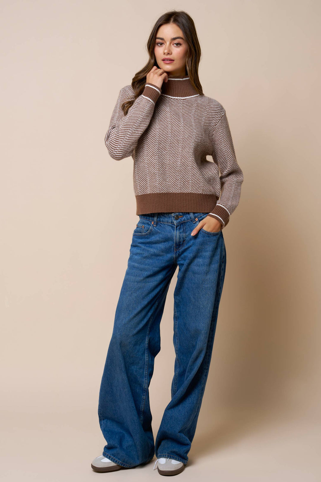 Woman wearing a brown patterned sweater and blue jeans against a beige background