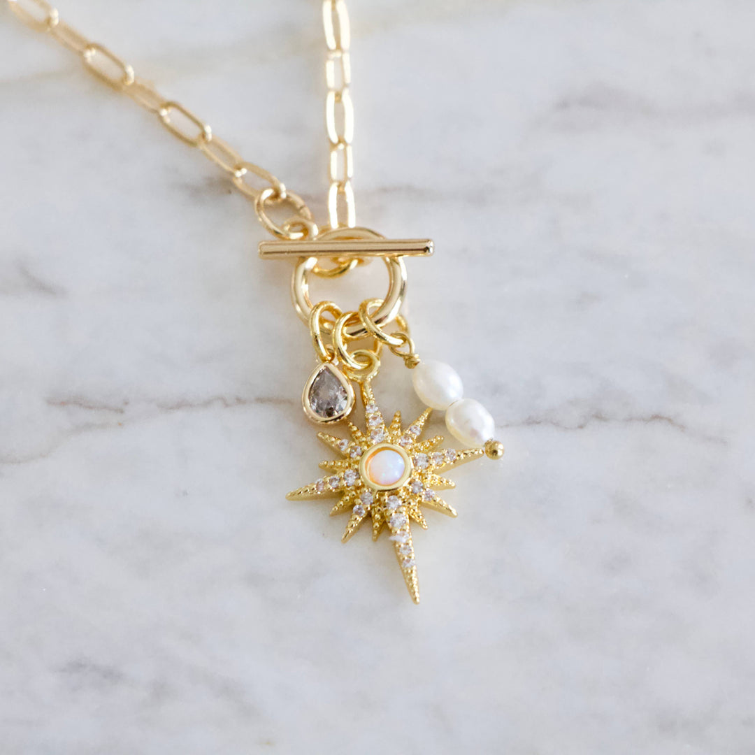 Gold necklace with star-shaped pendant and toggle clasp on a marble background