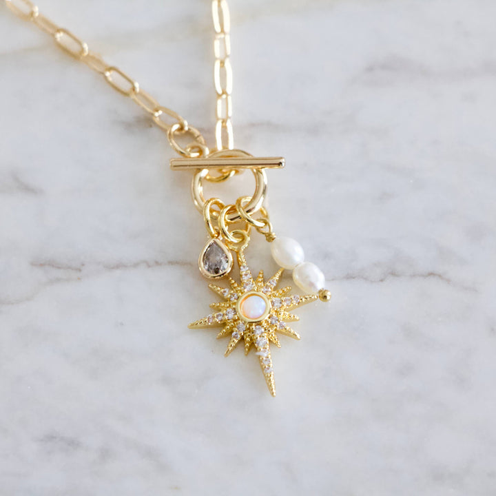Gold necklace with star-shaped pendant and toggle clasp on a marble background