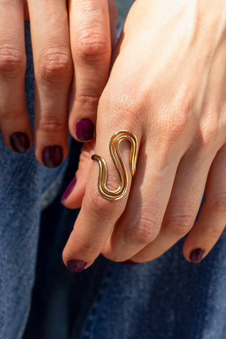 Gold wavy ring on a finger with a blurred blue background
