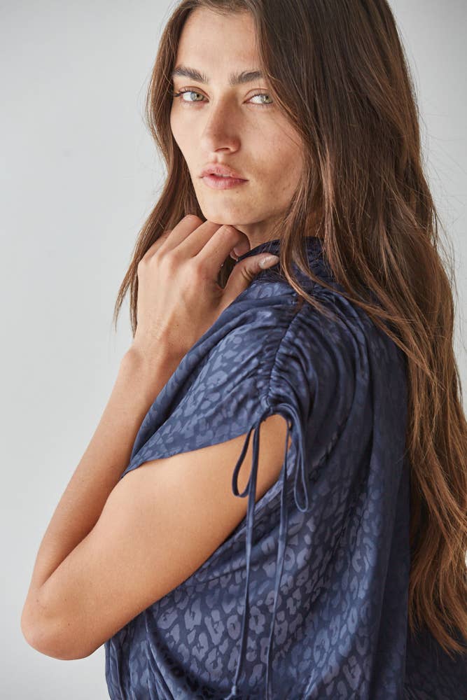 A woman wearing a dark blue animal print patterned short-sleeve top with side cutouts and drawstrings, photographed against a light gray studio background.