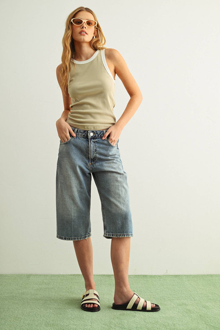 Woman wearing a beige ribbed tank top and blue denim shorts against a white background.
