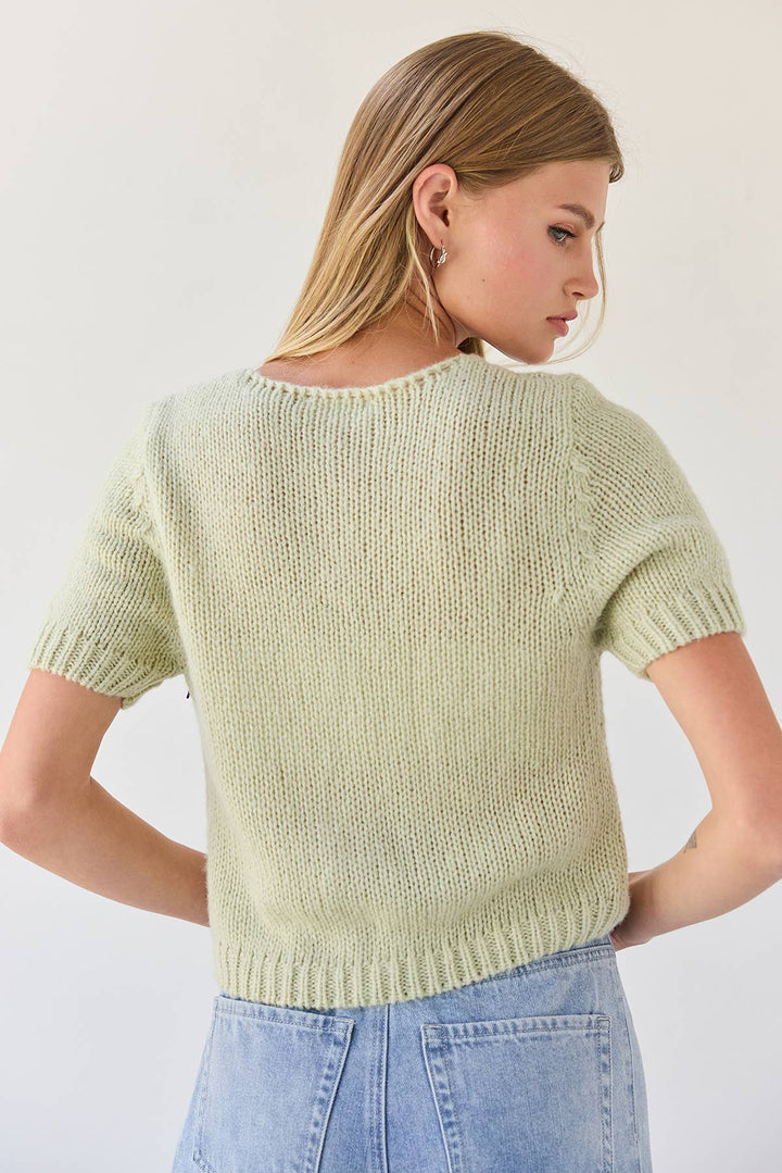 Woman wearing a light green knitted sweater and blue jeans against a white background