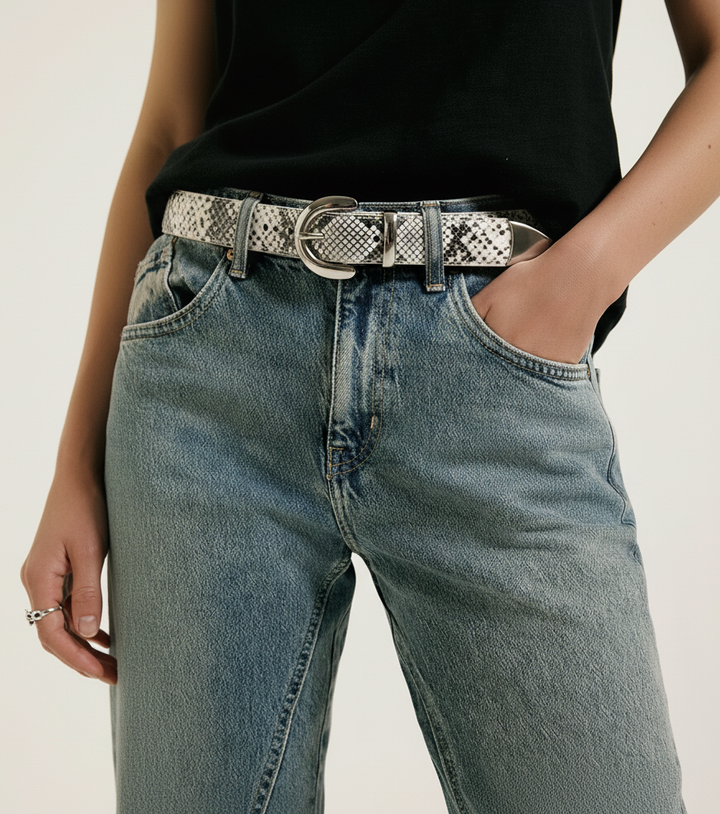 Woman wearing blue jeans with a snake skin leather belt with silver buckle on a plain background