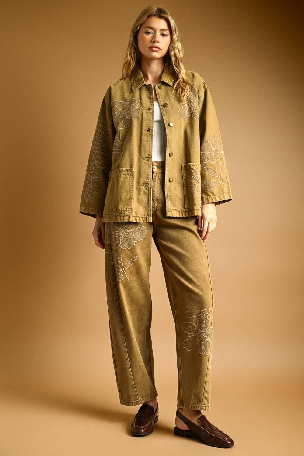 Woman wearing a tan denim jacket with matching denim pants on a beige background