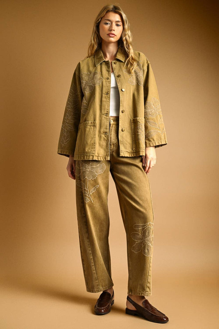 Woman wearing a tan denim jacket with matching denim pants on a beige background