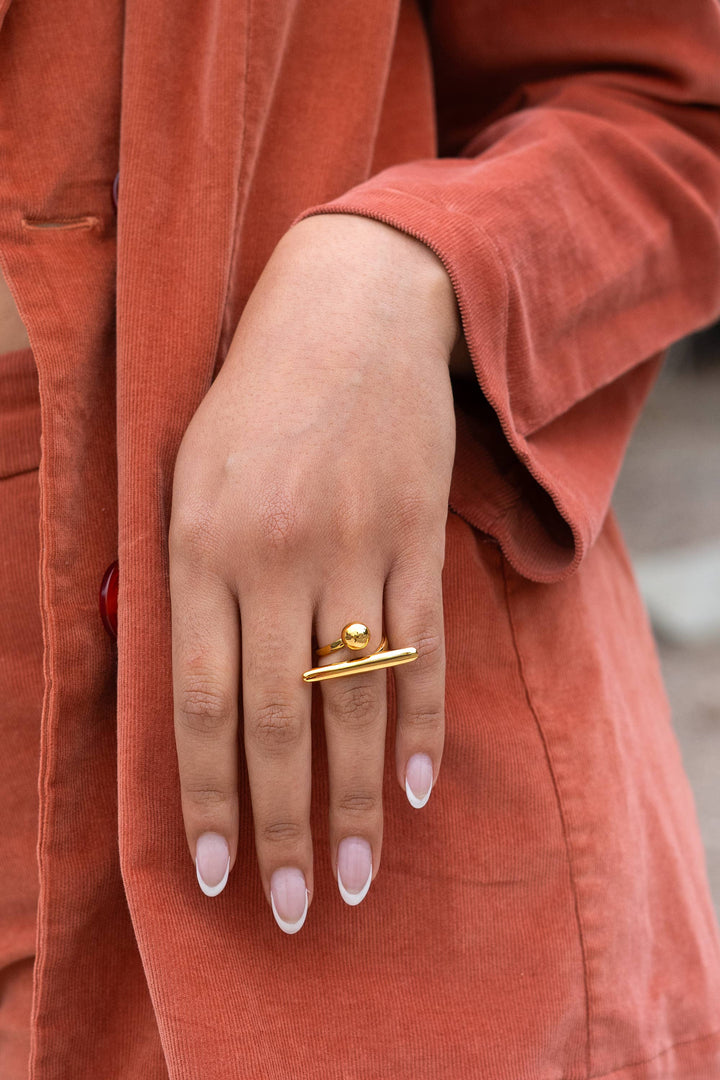 Close-up of a hand wearing a gold adjustable ring with a rust-colored coat in the background