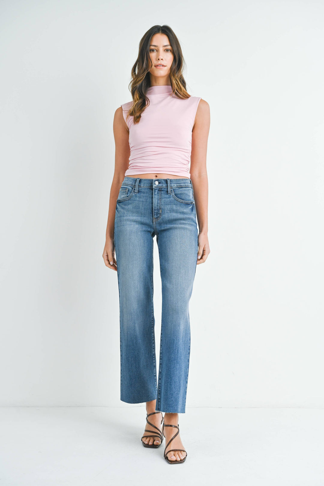 Woman wearing a pink sleeveless top and blue jeans on a white background