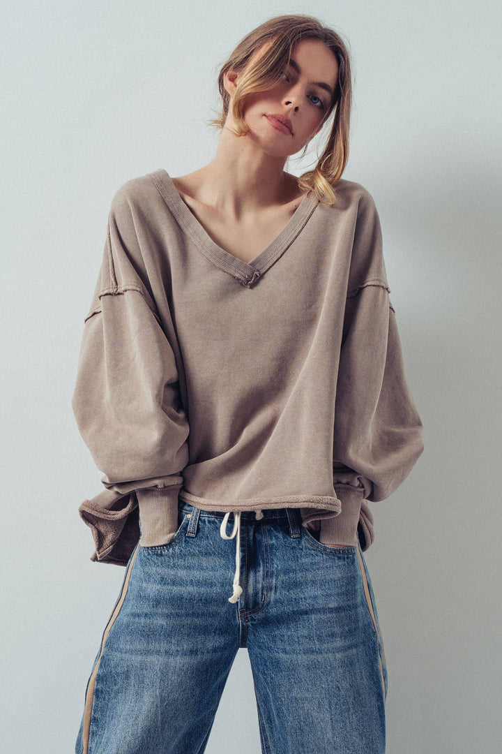 Woman wearing a beige oversized sweatshirt and blue jeans against a plain background