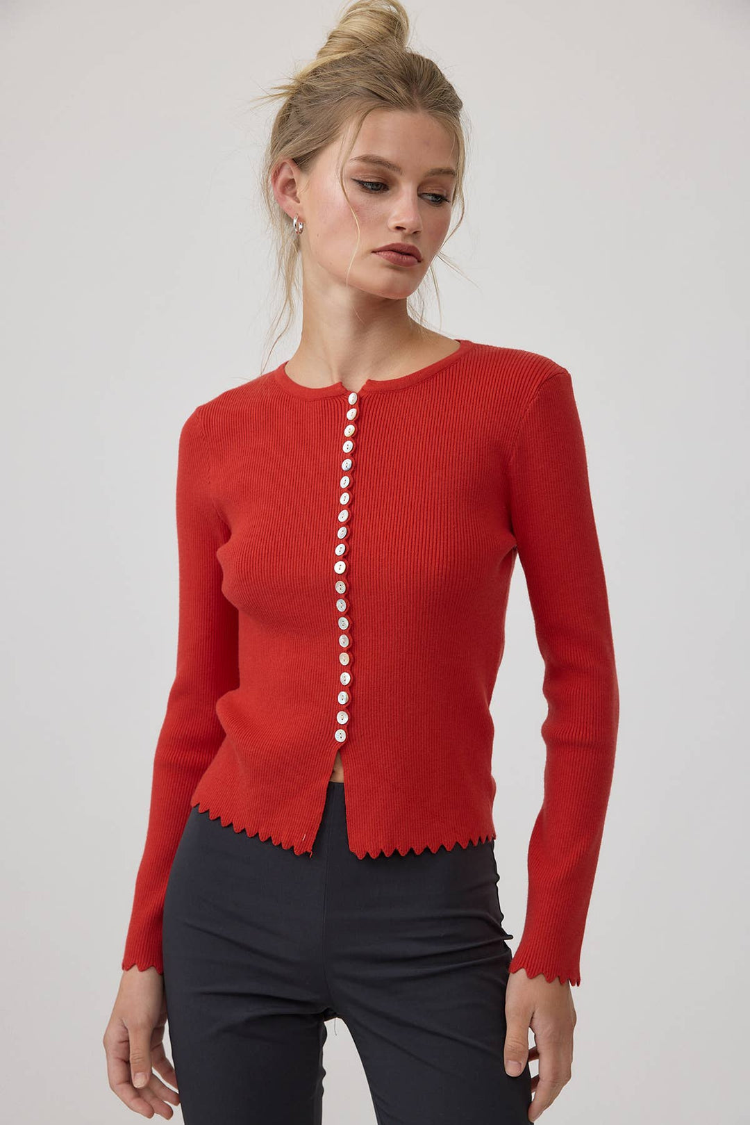Woman wearing a red cardigan with white buttons on a plain background
