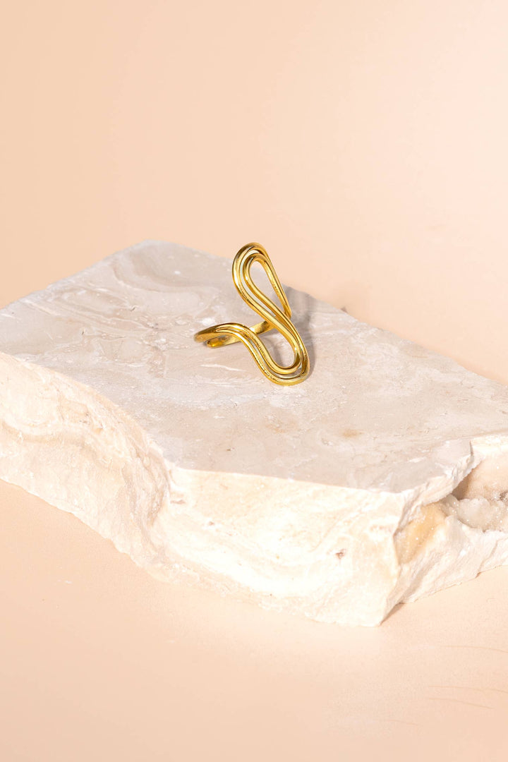 Gold spiral ring on a marble surface with a beige background