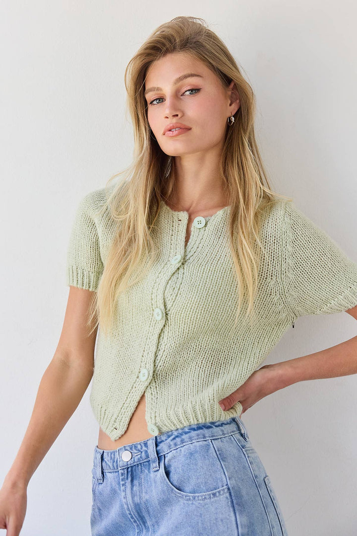 Woman wearing a light green knitted cardigan and blue jeans against a white background