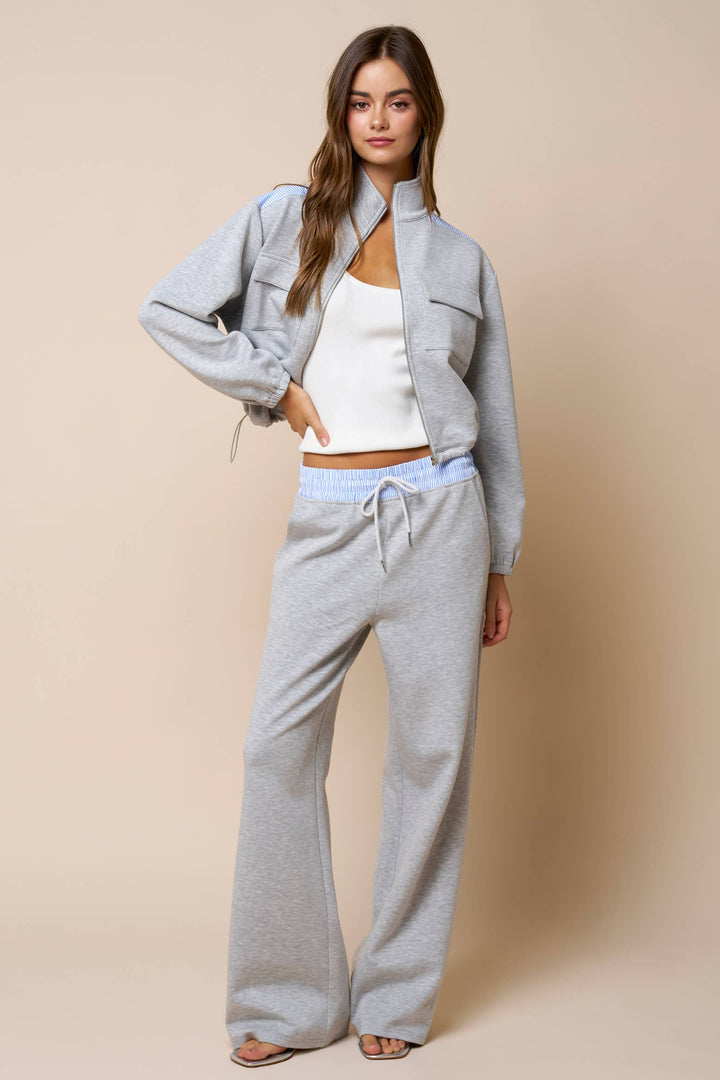 Woman wearing a light gray sweatshirt jacket and gray lounge wear pants with a white top against a beige background