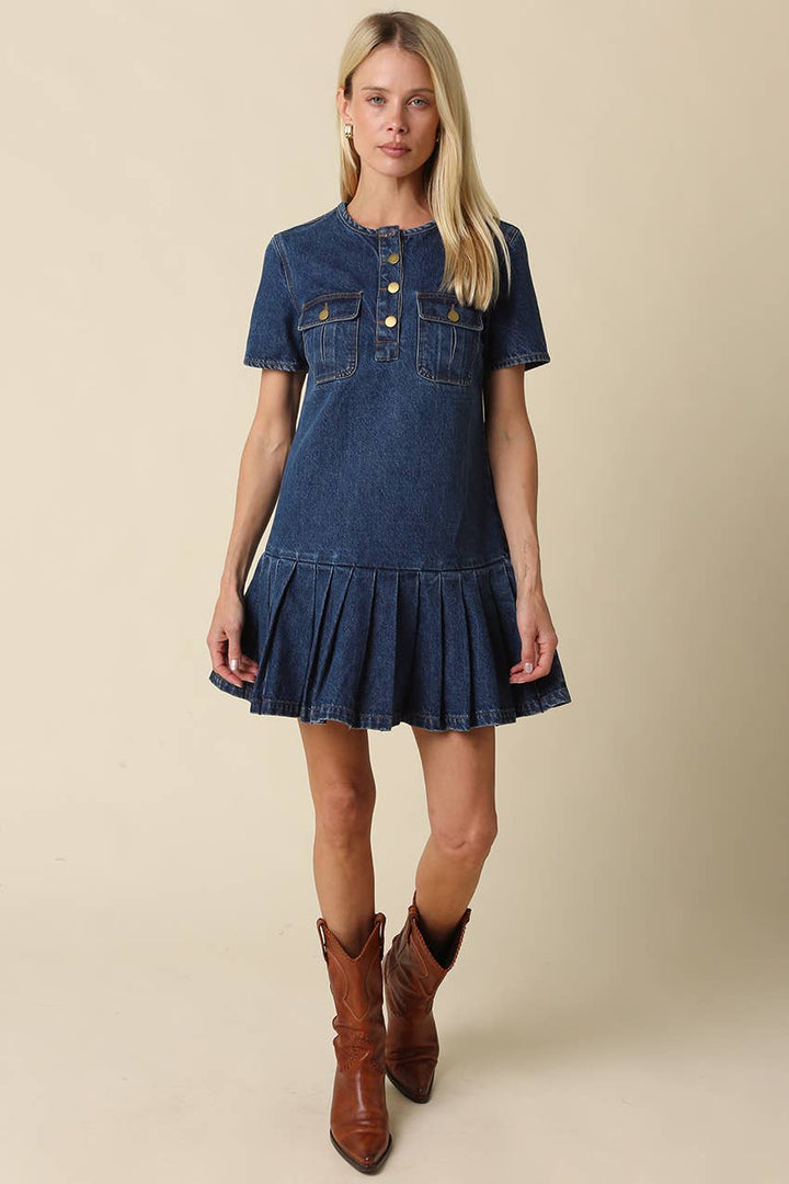 Woman wearing a short sleeve dark wash denim mini dress with brown boots on a beige background