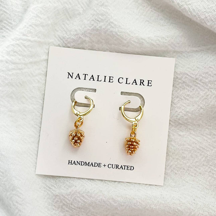 Gold earrings with pinecone charms on a 'Natalie Clare' card.