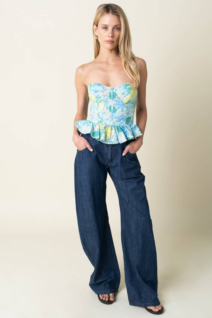 Woman wearing a strapless floral top with peplum waist and wide-leg jeans on a plain background